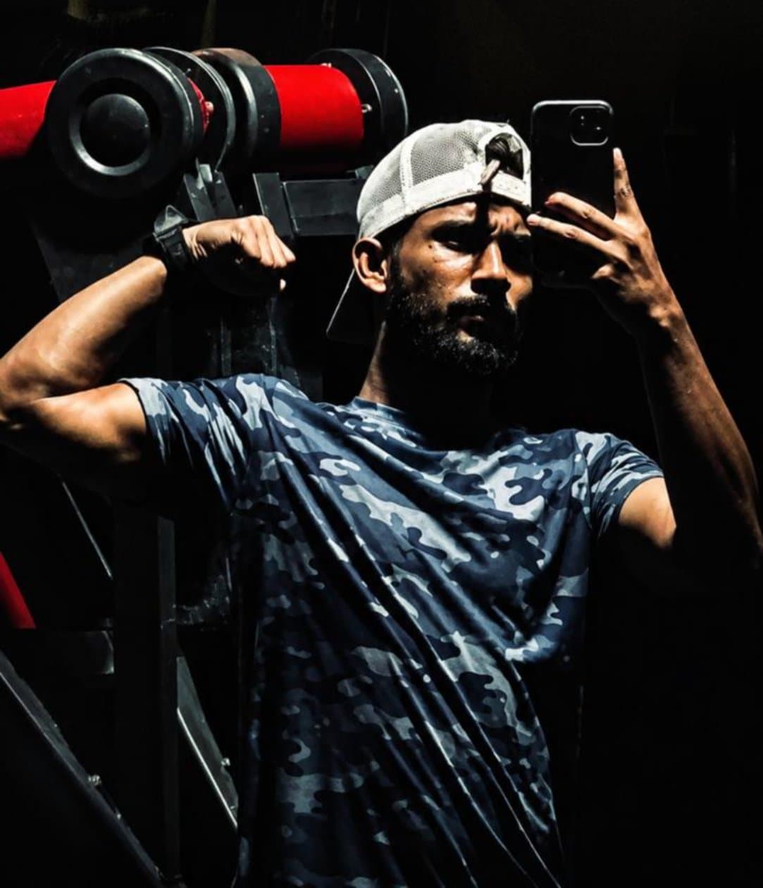 Saku Jeackz in a dark gym, taking a mirror photo beside a weight machine